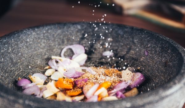 Fresh spices and onions being prepared in a stone mortar